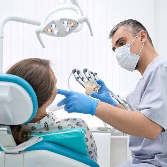 Dental professional in mask and gloves demonstrates a dental model to patient in bright clinic setting